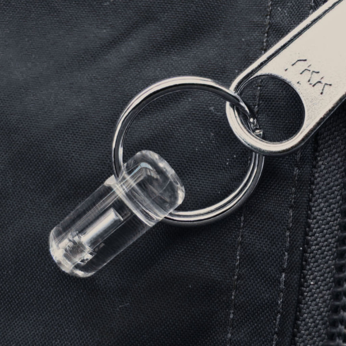 Close-up of Firefly Zip Marker with clear housing and metal split ring attached to a bag zip