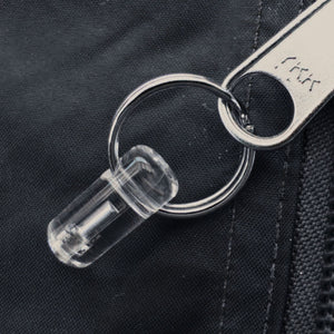 Close-up of Firefly Zip Marker with clear housing and metal split ring attached to a bag zip